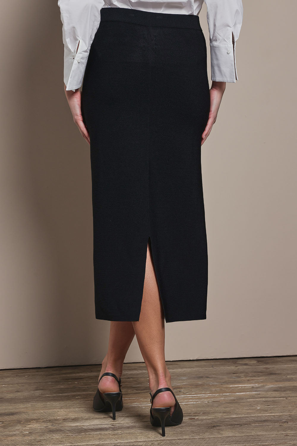 Model Madeline wearing size S of The Crepe Knit Multiway Pull On Skirt in colour Black (Black), from the back