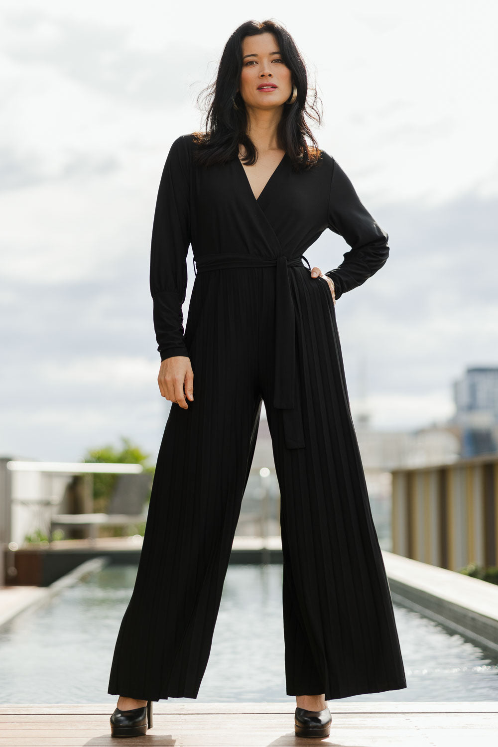 Model Miranda wearing size 10 of The Pleated Wide Leg Jumpsuit in colour Black (Black), from the front, showing the whole outfit