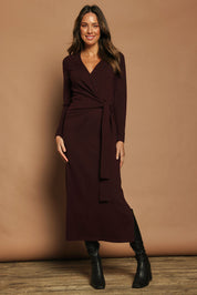 Model Madeline wearing size S of The Tie Waist Faux Wrap Knit Dress in colour Burntplum (Purple), from the front, showing the whole outfit