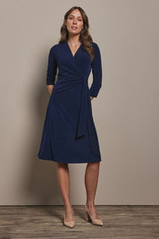 Model Madeline wearing size 10 of The Tie Waist Dress in colour Navy (Blue), from the front, showing the whole outfit