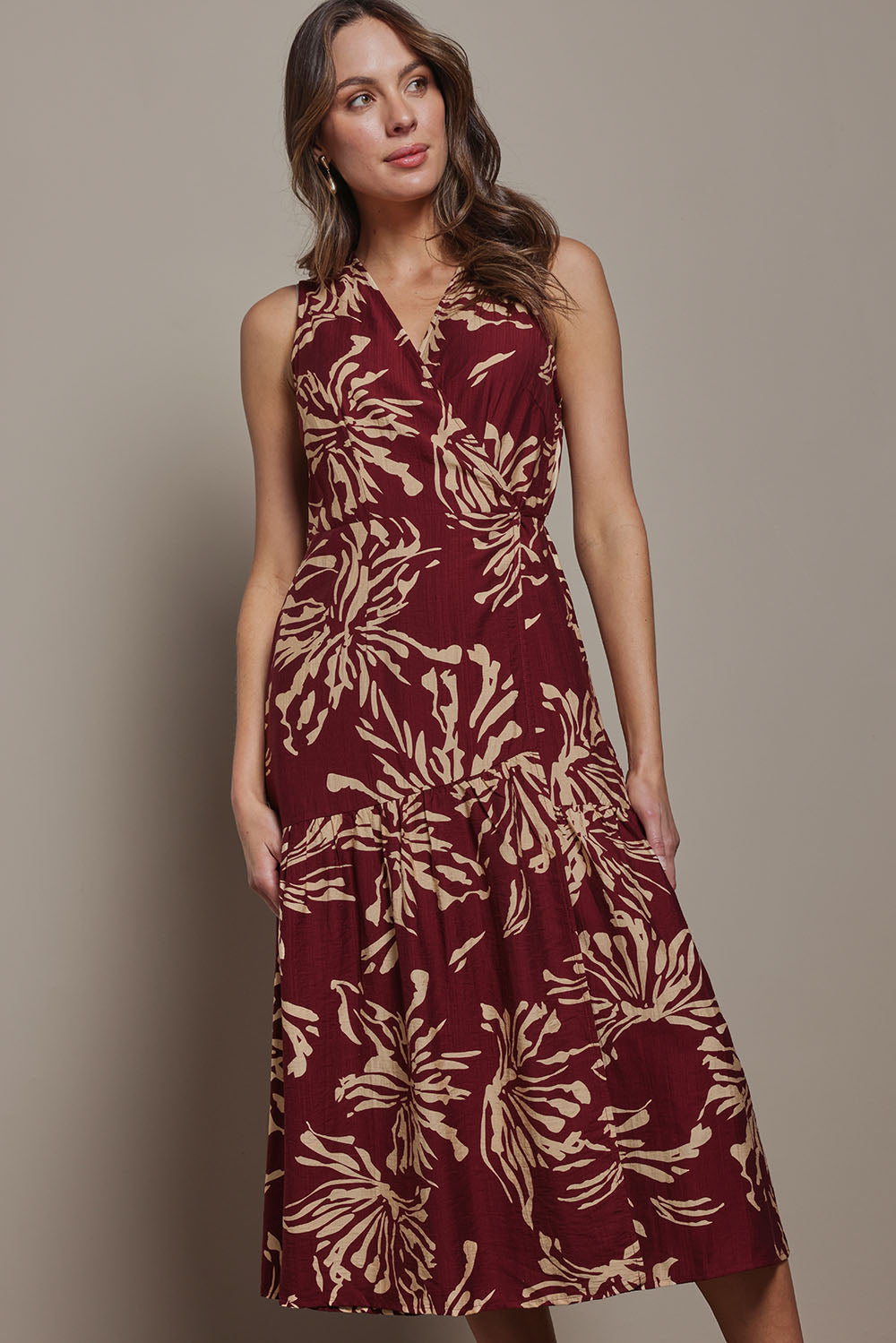 Model Madeline wearing size 10 of The Printed Sleeveless Wrap Dress in colour Winefleur (Red), from the front, cropped image