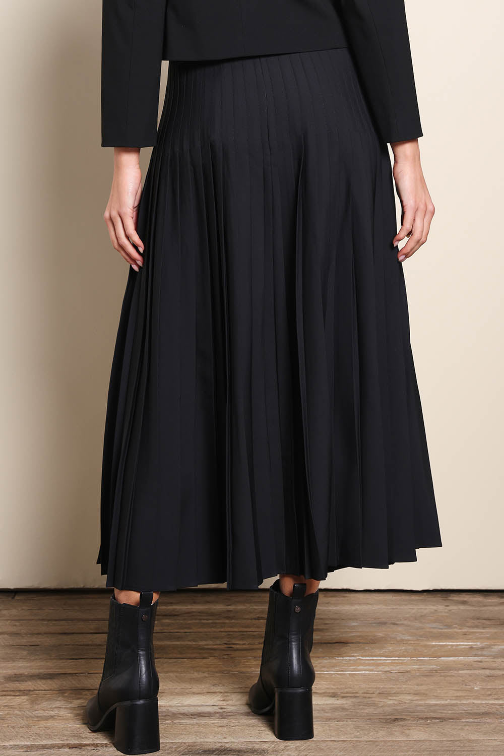 Model Madelinec wearing size 10 of the The Luxe Pleated Skirt – Black in colour Black, from the back