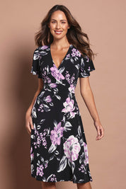 Model Madeline wearing size 10 of The Printed Jersey Faux Wrap Dress in colour Pinkfloral (Black), from the front, cropped image