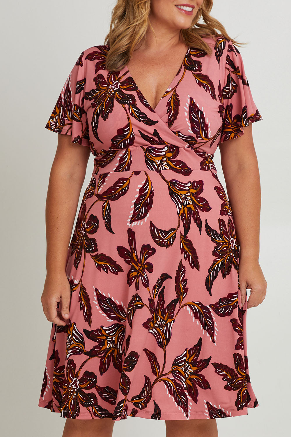 Model Fiona wearing size 16 of The Printed Jersey Faux Wrap Dress in colour Pinkfleur (Pink), from the front, cropped image