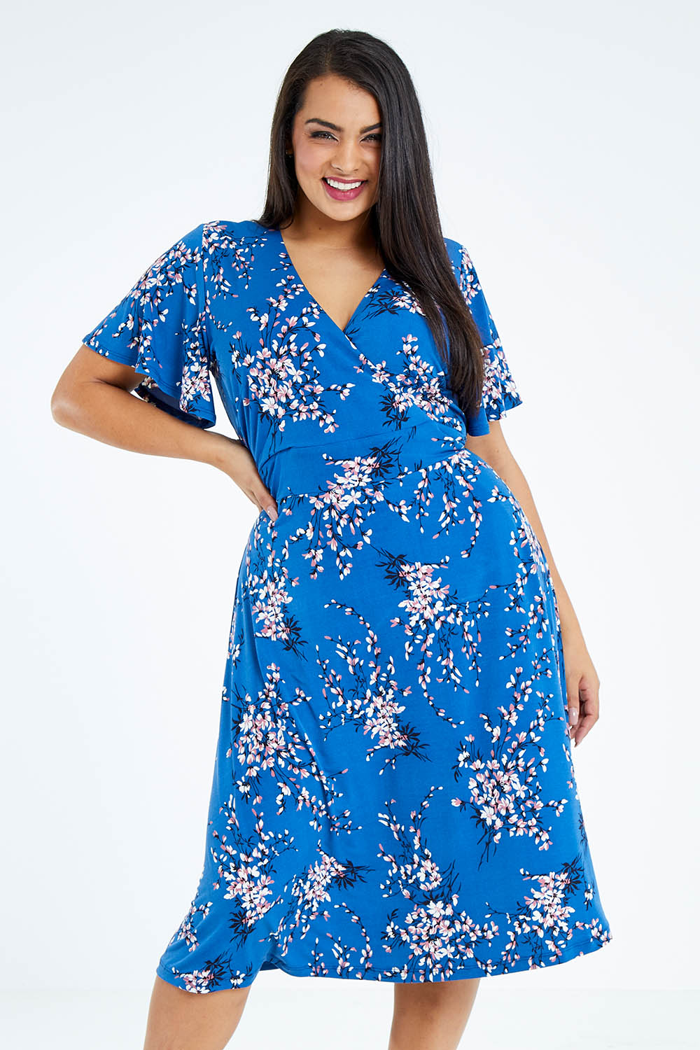 Model Sasha-Lee wearing size 16 of The Printed Jersey Faux Wrap Dress in colour Blossom (Blue), from the front, cropped image