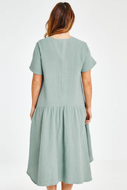 Model Laura wearing size 12 of the Belle Angled Hem Dress in colour Sage (Green), from the back