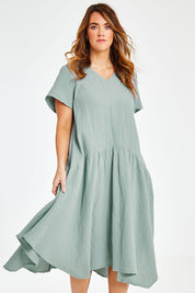 Model Laura wearing size 12 of the Belle Angled Hem Dress in colour Sage (Green), from the front, cropped image