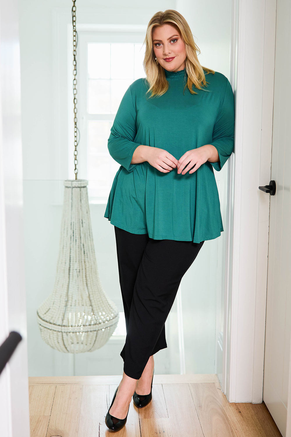 Model Caitlin wearing size 18 of the Belle Turtleneck Draped Bamboo Tee in colour Teal (Green), from the front, showing the whole outfit