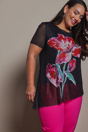 Model Ashleigh wearing size 16 of the Belle Printed Mesh Asymmetric Tee in colour Blackfleur (Black), from the front, cropped image