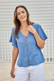 Model Tegand wearing size 10 of the Cute As A Button Blouse – Denim in colour Denim, in a cropped view