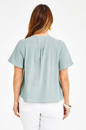 Model Laura wearing size 14 of the Cute As A Button Blouse in colour Sage (Green), from the back