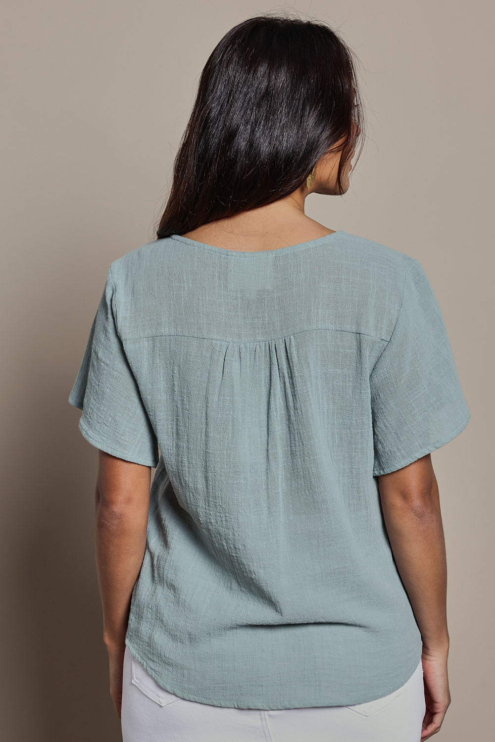Model Tahnee wearing size 10 of the Cute As A Button Blouse in colour Sage (Green), from the back