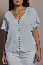 Model Tahnee wearing size 10 of the Cute As A Button Blouse in colour Sky (Blue), from the front, cropped image
