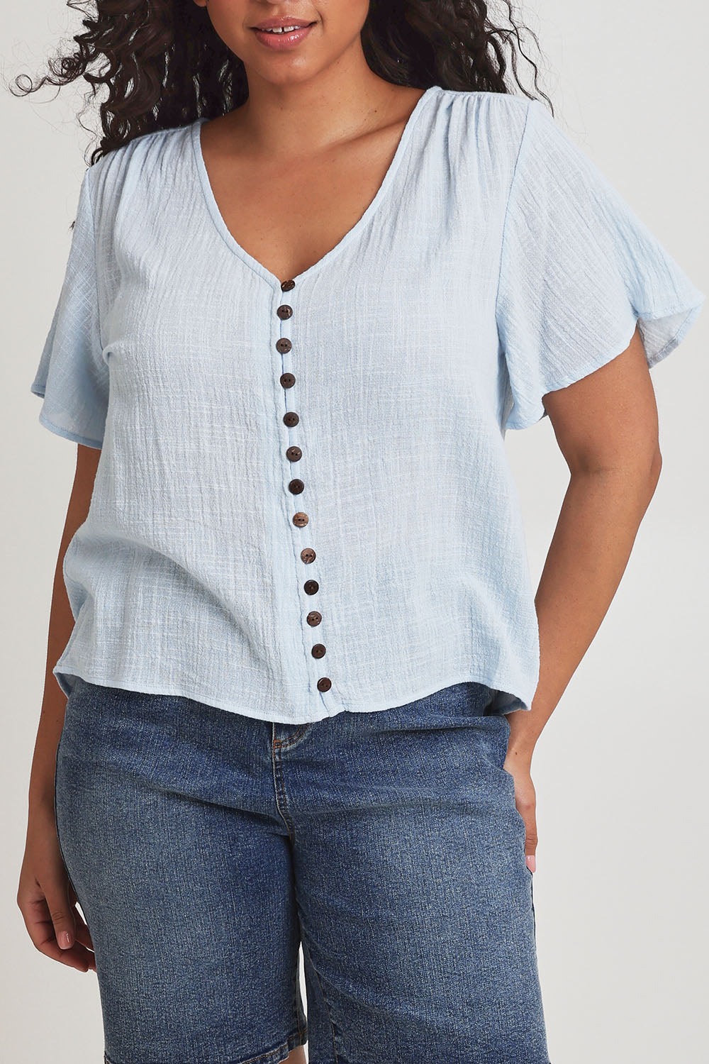 Model Terri-Leigh wearing size 14 of the Cute As A Button Blouse in colour Sky (Blue), from the front, cropped image