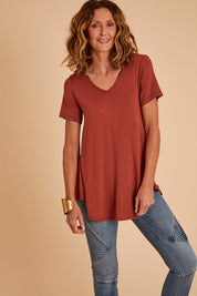 Model Emma wearing size 10 of the Softly Swinging Bamboo Tee in colour Clay (Red), from the front, cropped image