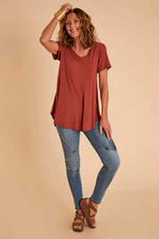 Model Emma wearing size 10 of the Softly Swinging Bamboo Tee in colour Clay (Red), from the front, showing the whole outfit
