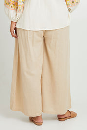 Model Monique wearing size 14 of the Serene Day Wide Leg Pants in colour Sand, from the back