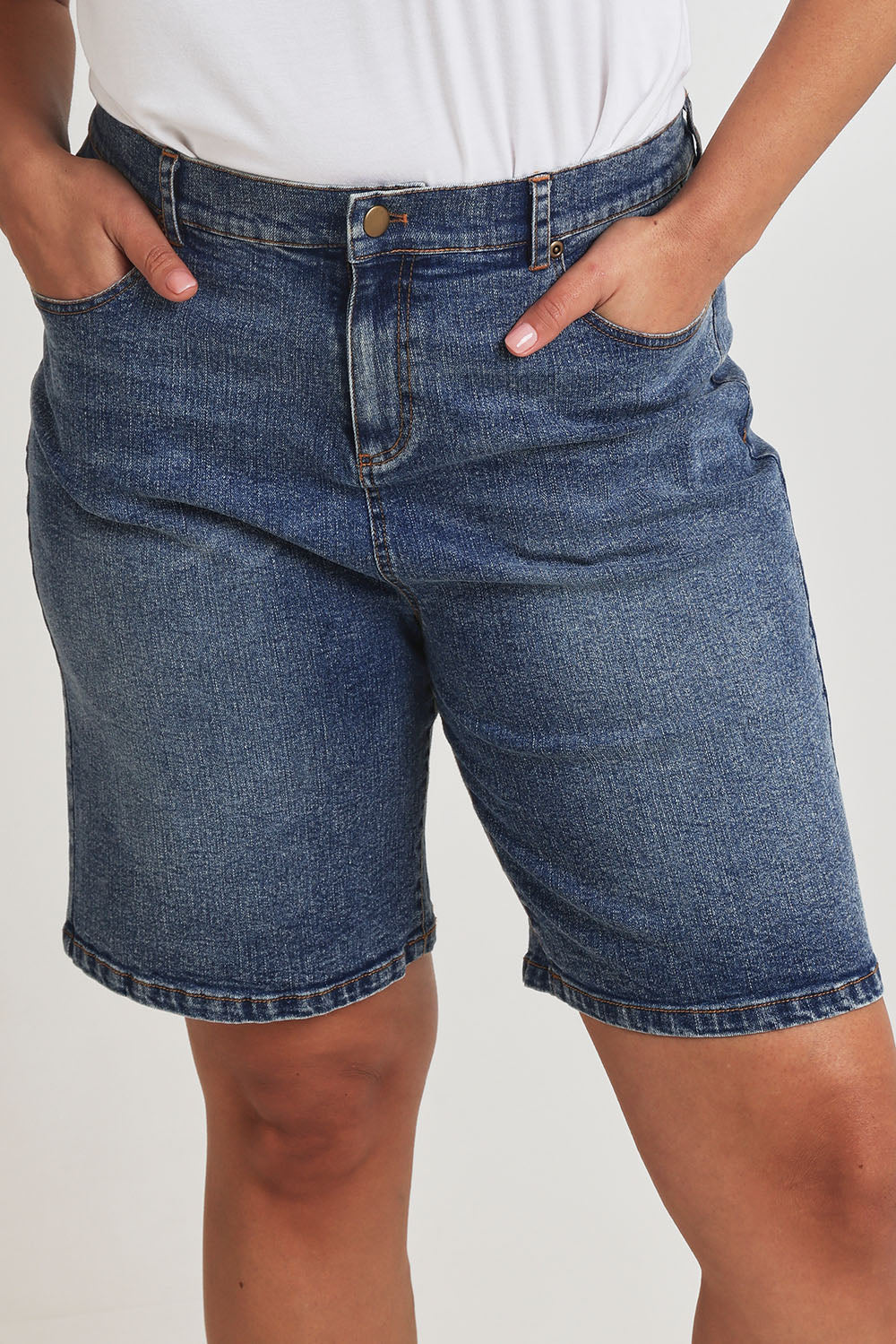 Model Terri-Leigh wearing size 14 of the Daily Dose Longline Denim Shorts in colour Denim (Blue), from the front, cropped image