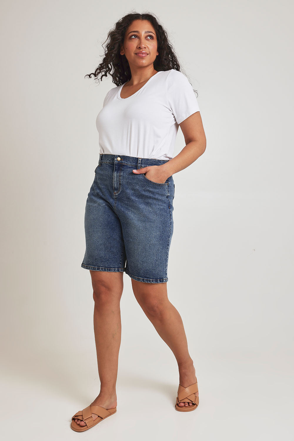 Model Terri-Leigh wearing size 14 of the Daily Dose Longline Denim Shorts in colour Denim (Blue), from the front, showing the whole outfit