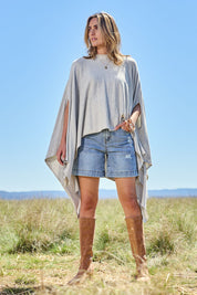 Model Tegan wearing the Light Breeze Poncho in colour Mist (Grey), from the front, showing the whole outfit