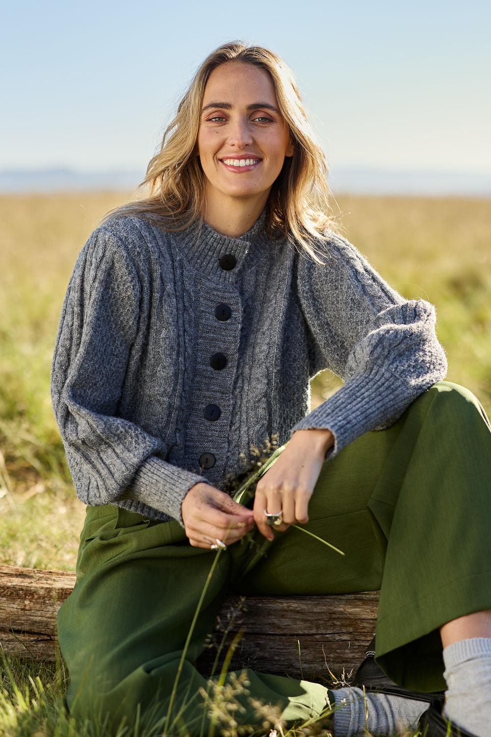 Model Tegan wearing size S of the Level Up Cropped Cable Cardi in colour Smoke (Grey), from the front, showing the whole outfit