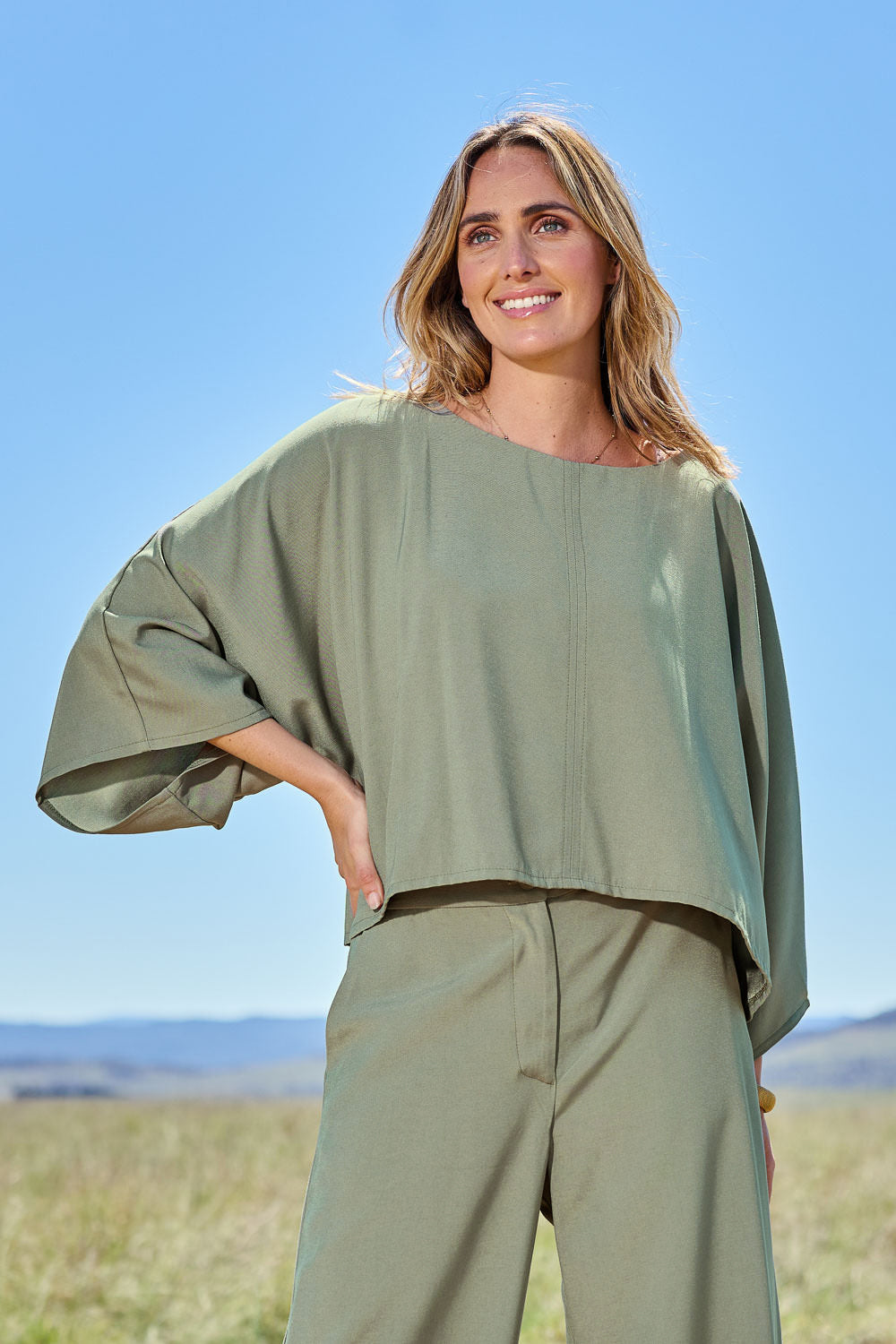 Model Tegan wearing size 10 of the Striding Out Kimono Sleeve Top in colour Thyme (Green), from the front, showing the whole outfit