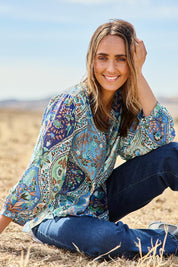 Model Tegan wearing size 10 of the Easy On Me Blouse in colour Bluefolk (Blue), from the front, showing the whole outfit