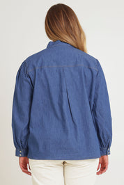 Model Chanel wearing size 16 of the Take A Bow Chambray Blouse in colour Demin (Blue), from the back