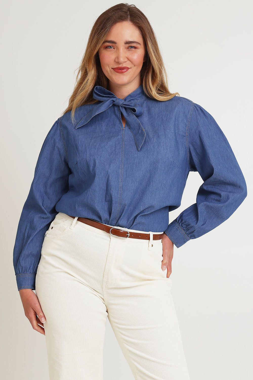Model Chanel wearing size 16 of the Take A Bow Chambray Blouse in colour Demin (Blue), from the front, cropped image