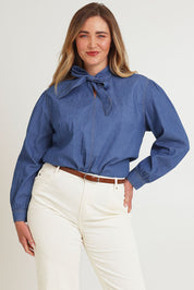 Model Chanel wearing size 16 of the Take A Bow Chambray Blouse in colour Demin (Blue), from the front, cropped image