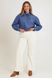 Model Chanel wearing size 16 of the Take A Bow Chambray Blouse in colour Demin (Blue), from the front, showing the whole outfit