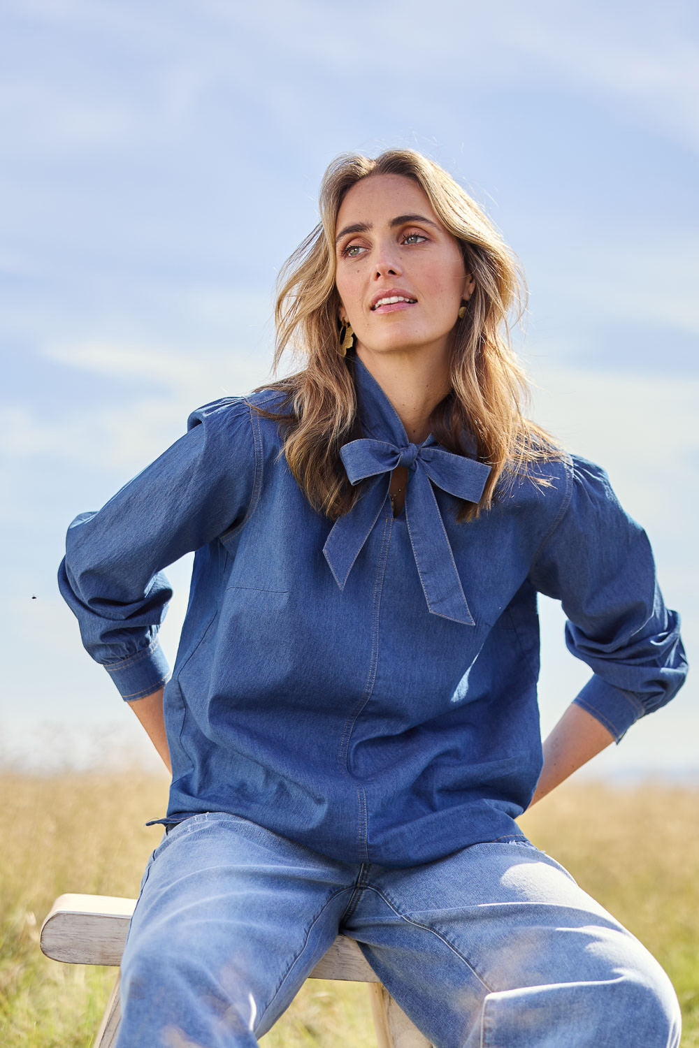 Model Tegan wearing size 10 of the Take A Bow Chambray Blouse in colour Demin (Blue), from the front, showing the whole outfit