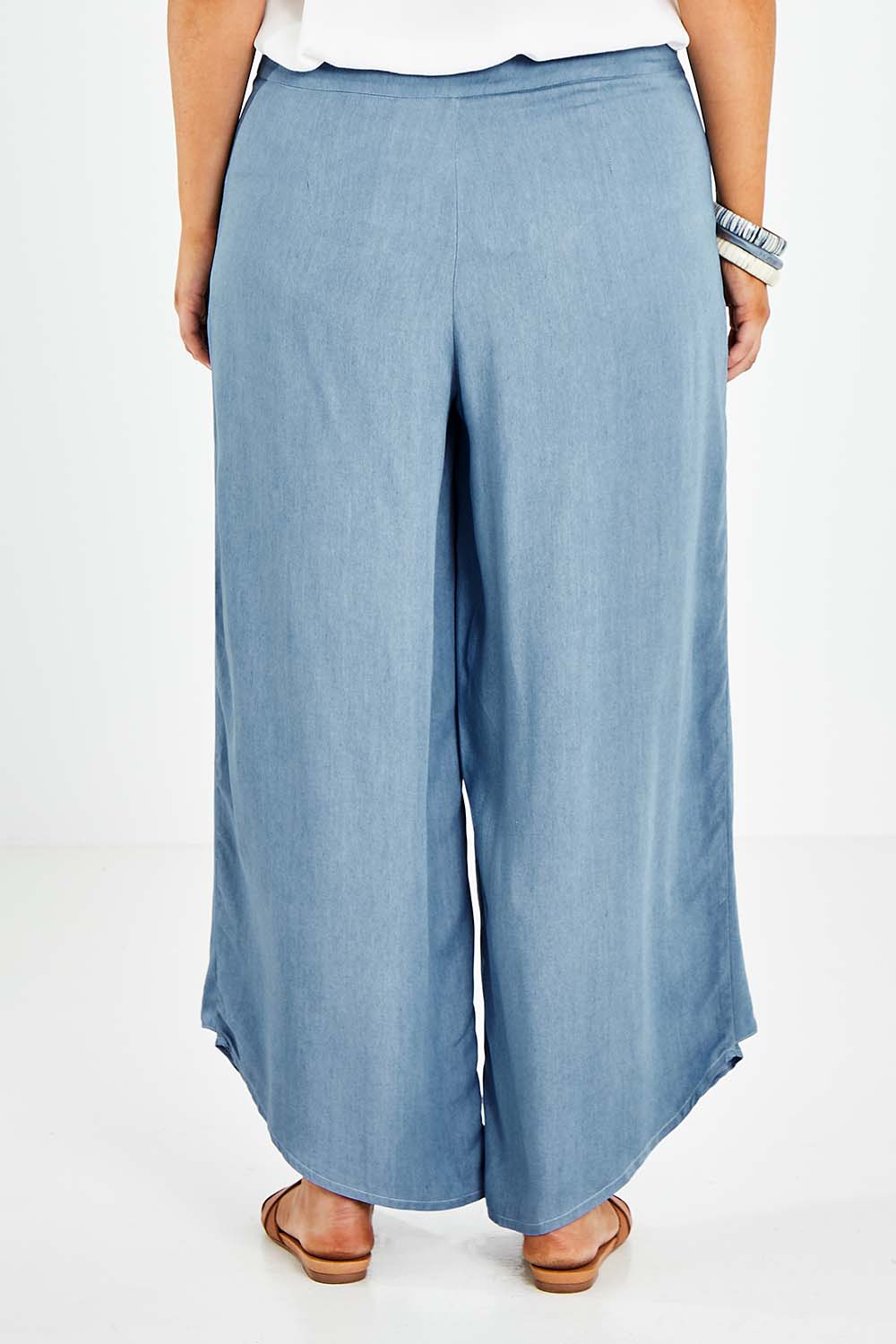 Model Jess wearing size 14 of the Wrapped In You Pants in colour Denim (Blue), from the back