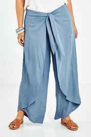 Model Jess wearing size 14 of the Wrapped In You Pants in colour Denim (Blue), from the front, cropped image