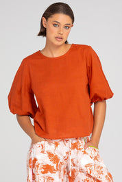 A model wearing the Ava Cotton Top in colour Mecca, from the front, cropped image