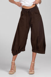 A model wearing the Guru Pant in colour Coffee, from the front, cropped image