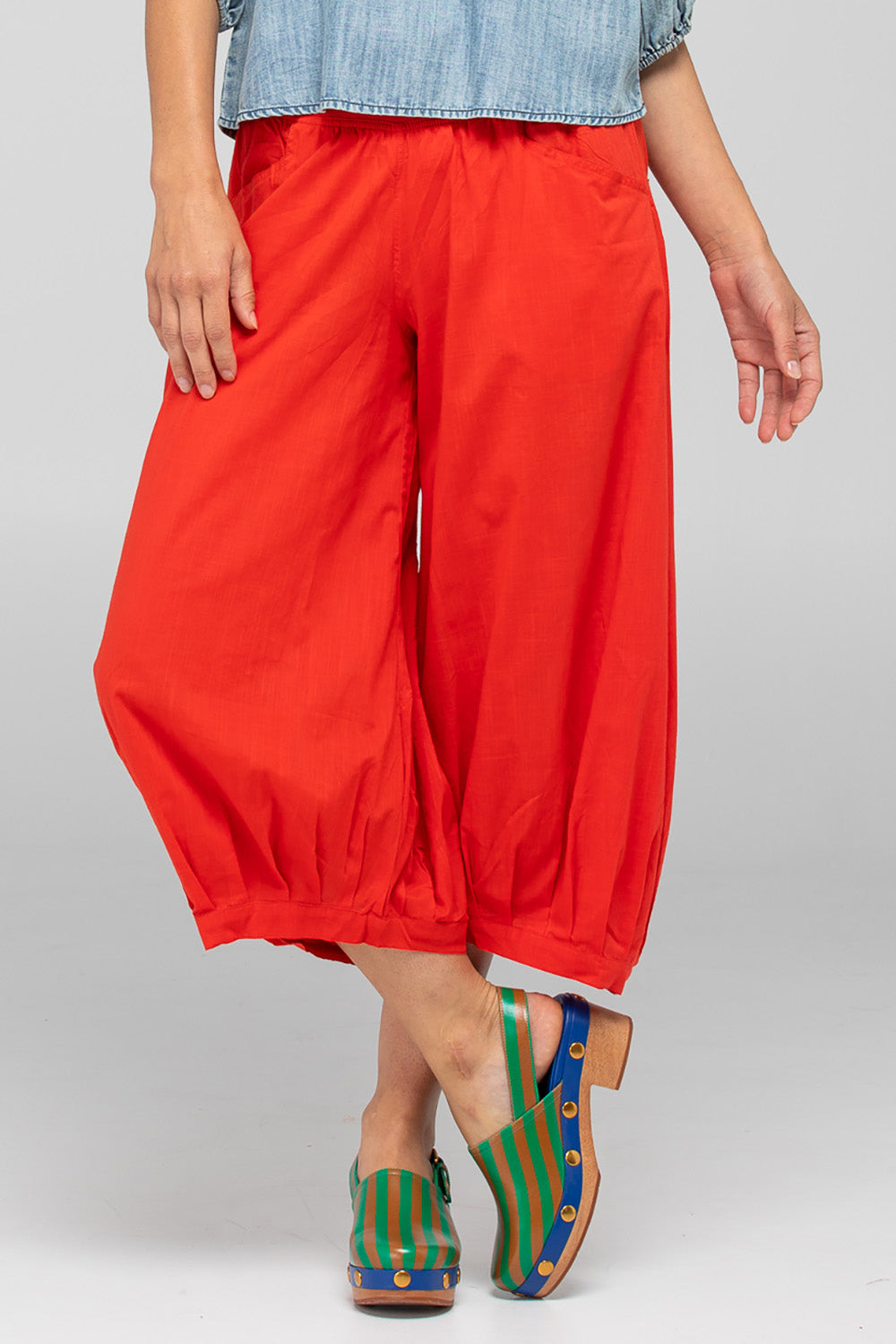 A model wearing the Guru Cotton Pant in colour Pomodoro (Red), from the front, cropped image