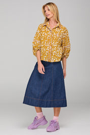 A model wearing the Pari Shirt in colour Mustard, from the front, showing the whole outfit