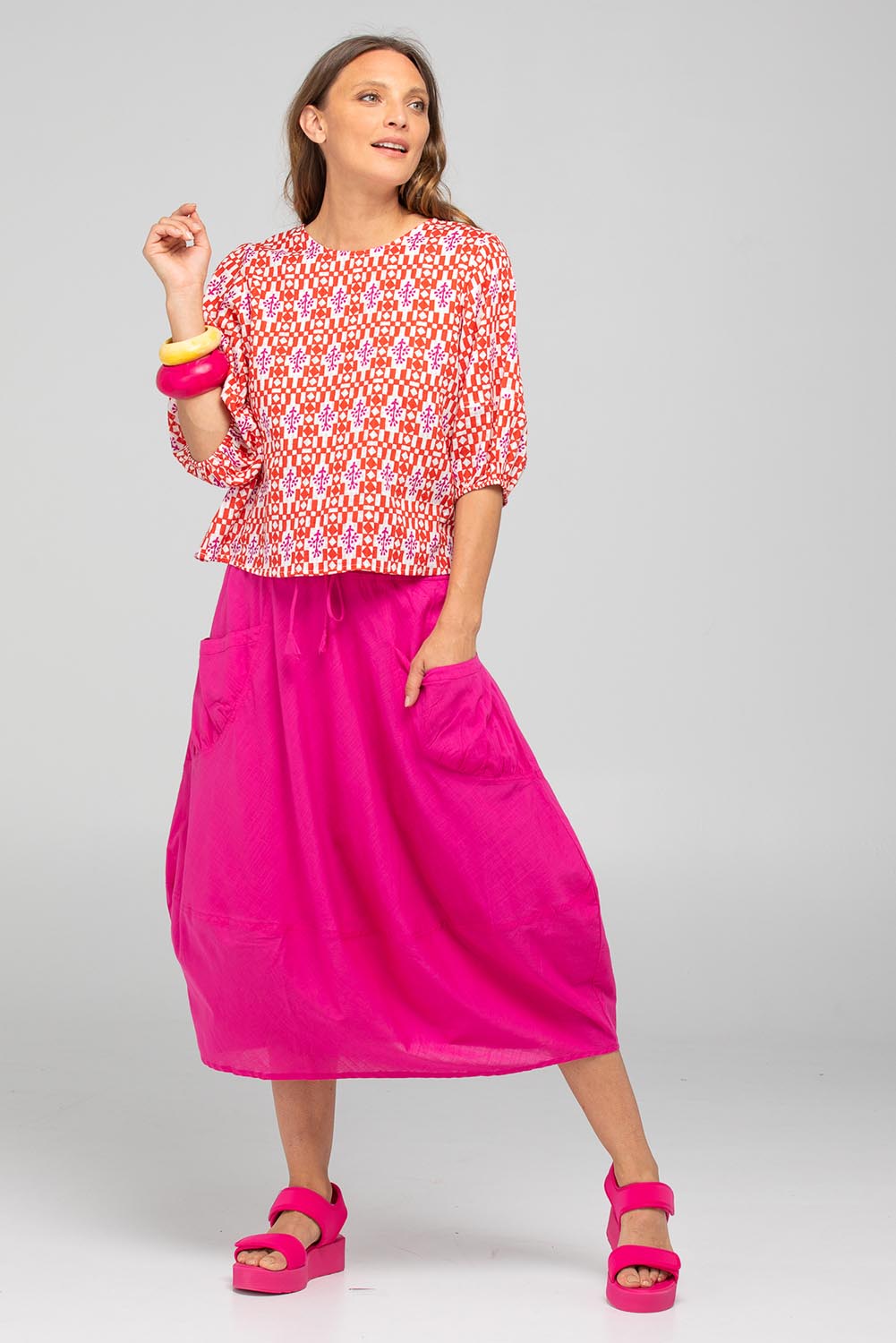 A model wearing the Guru Cotton Skirt in colour Fiore (Pink), from the front, showing the whole outfit