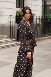A model wearing the Zion Dress in colour Stonespot (Black), from the front, showing the whole outfit