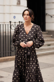 A model wearing the Zion Dress in colour Stonespot (Black), from the front, showing the whole outfit