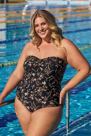 A model wearing the Twist Front Bandeau One Piece in colour Wildflower (Black), from the front, showing the whole outfit