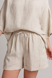 A model wearing the Studio Linen Short in colour Tusk, from the front, cropped image