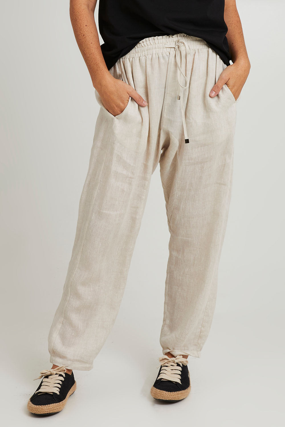 Model Katie wearing size S of the Studio Relaxed Linen Pant in colour Tusk, from the front, cropped image