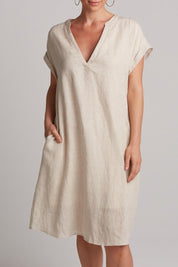 A model wearing the Studio Linen Dress in colour Tusk, from the front, cropped image