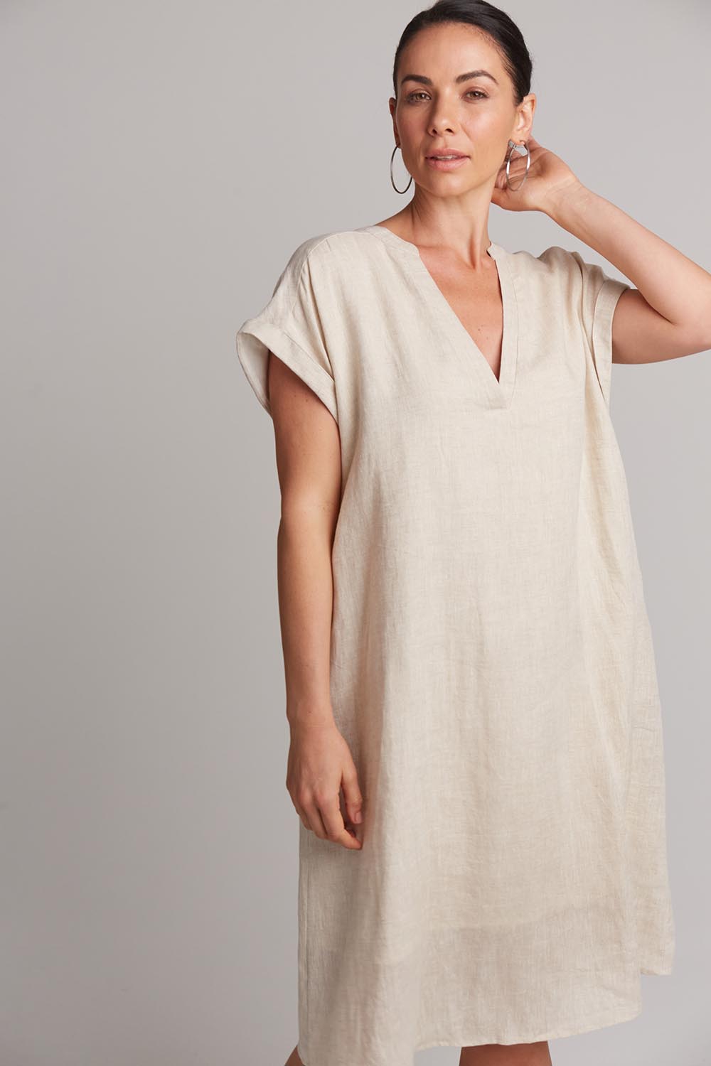 A model wearing the Studio Linen Dress in colour Tusk, from the front, cropped image