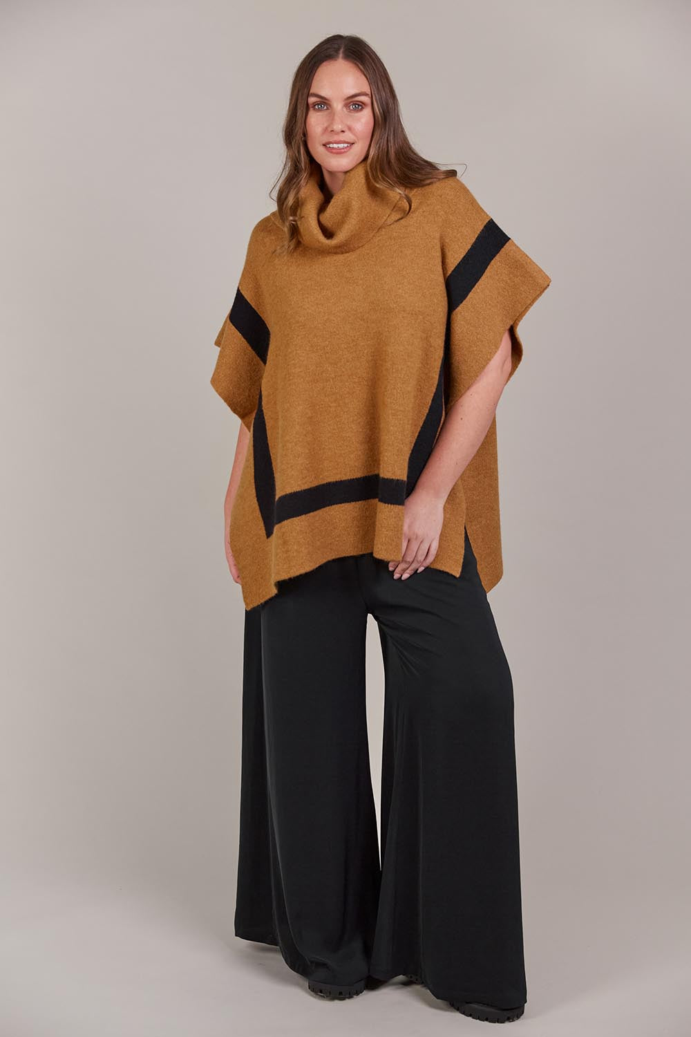 A model wearing the Avino Poncho in colour Tobacco, from the front, showing the whole outfit