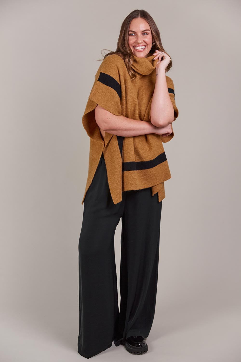 A model wearing the Avino Poncho in colour Tobacco, from the front, showing the whole outfit