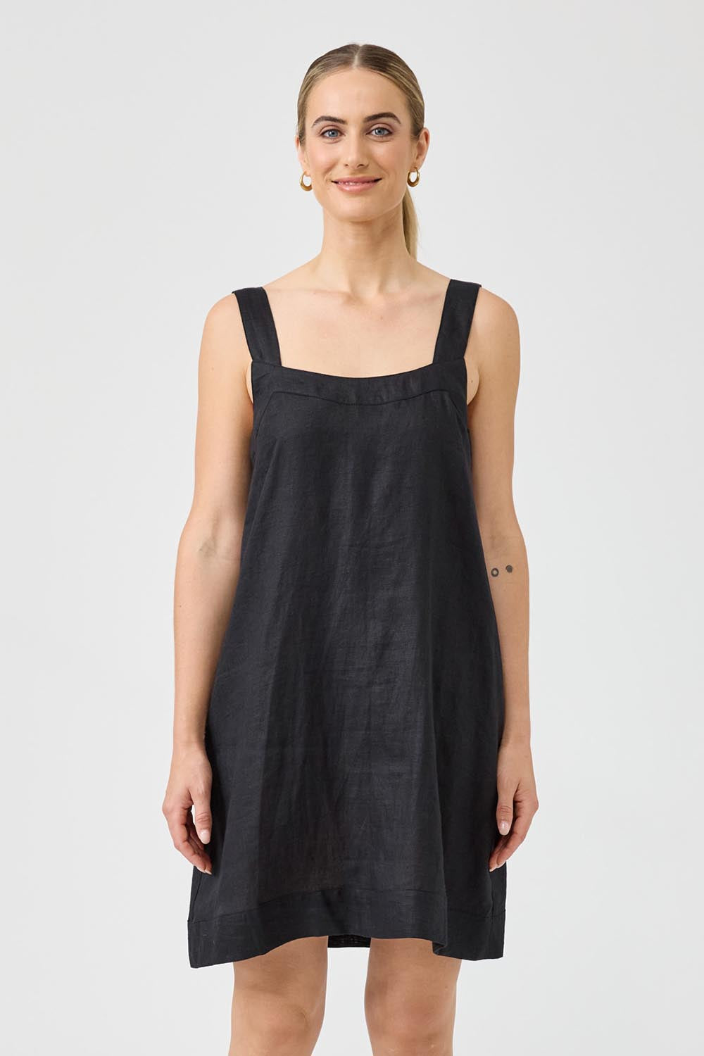 A model wearing the Studio Linen Short Tank Dress in colour Black (Black), from the front, cropped image