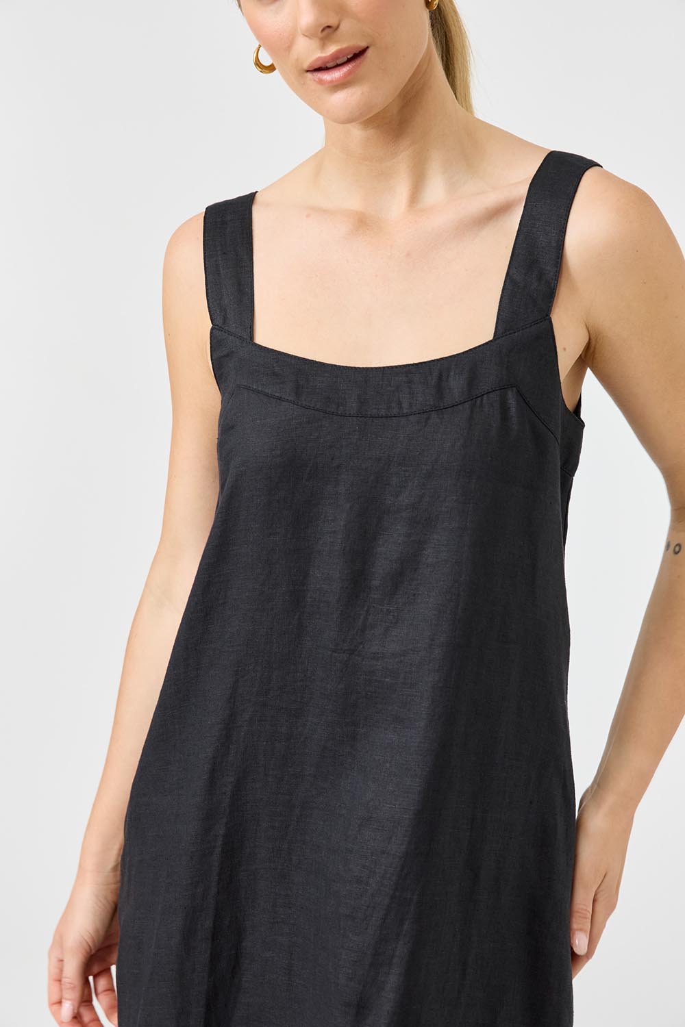 A model wearing the Studio Linen Short Tank Dress in colour Black (Black), from the front, cropped image
